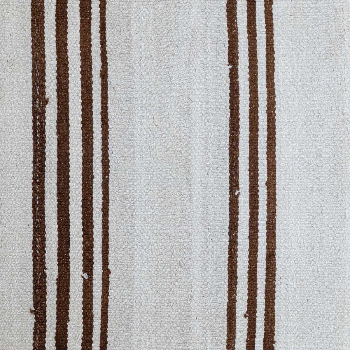 A close-up of a woven textile with a cream-colored background and vertical dark brown stripes.