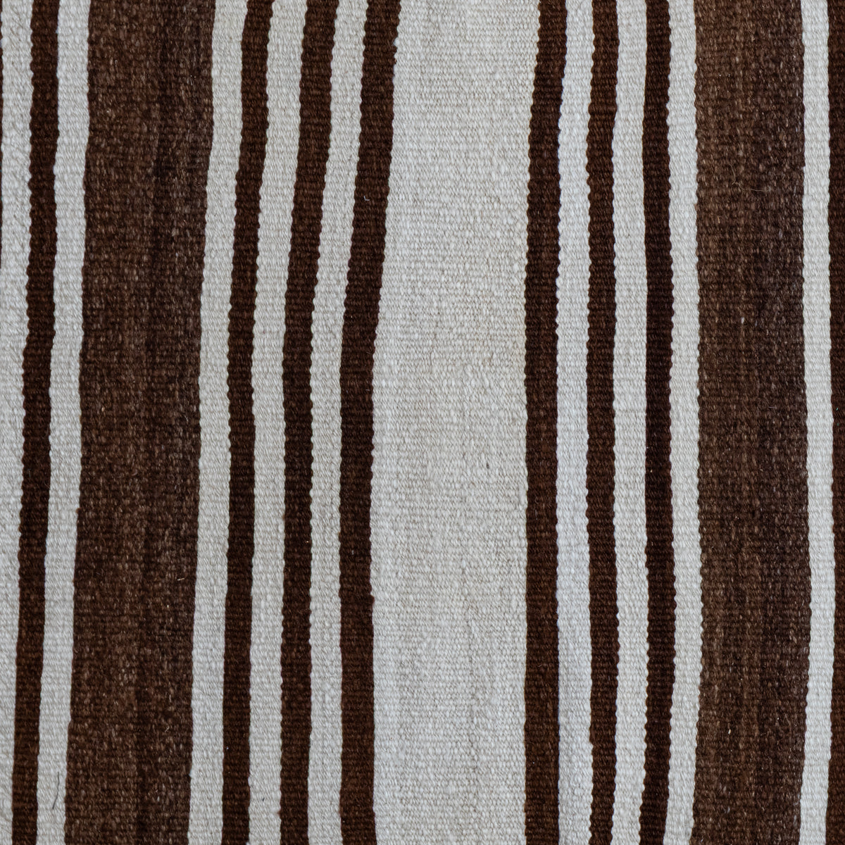 A close-up of a woven textile with vertical stripes in dark brown, medium brown, and off-white, showing a detailed texture.