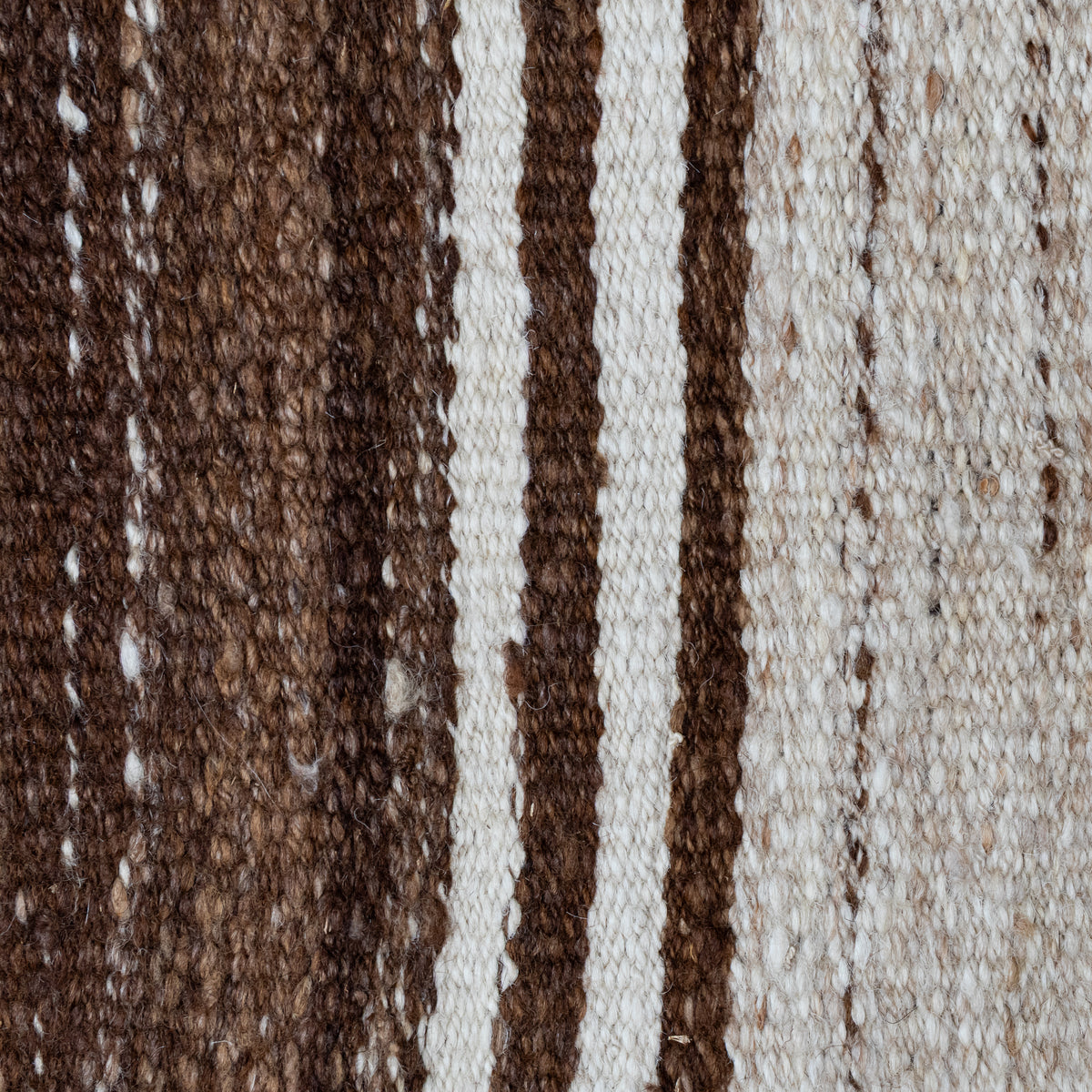 Close-up of a woven textile with vertical stripes in dark brown, medium brown, and off-white, showing the texture and material detail.