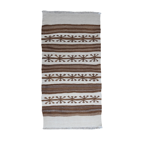 A rectangular woven textile with fringe on the top and bottom edges, featuring horizontal stripes in brown and off-white with geometric snowflake-like motifs, shown against a plain white background.