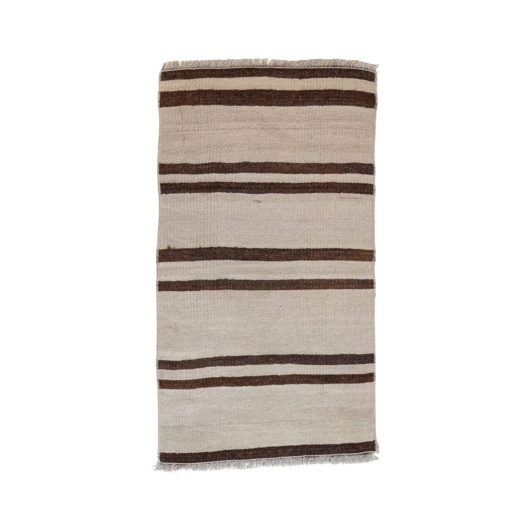 A rectangular woven rug with horizontal stripes in dark brown and beige, featuring fringed edges, shown against a plain white background.