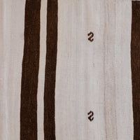 Close-up of a woven textile with a cream background, two wide dark brown vertical stripes, and two small dark brown zigzag motifs on the right side.