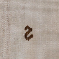 A close-up of a beige woven fabric with a small dark brown embroidered letter 's' in the center.