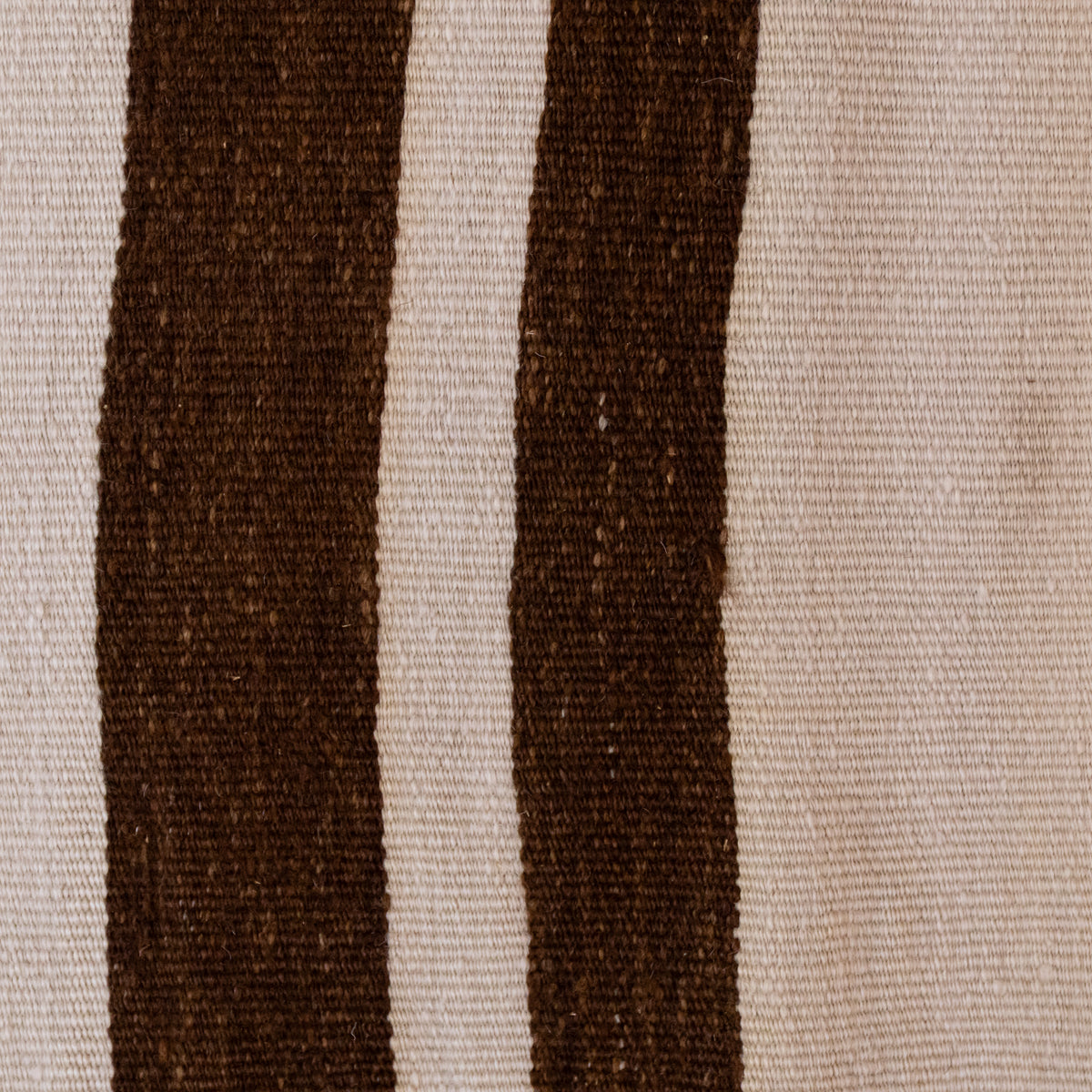 A close-up of a woven textile pattern featuring two vertical dark brown stripes on a warm beige background.