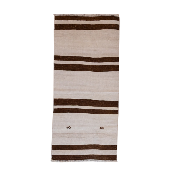 A rectangular woven rug with horizontal stripes in dark brown and cream, featuring small decorative motifs near the bottom center and fringed edges.