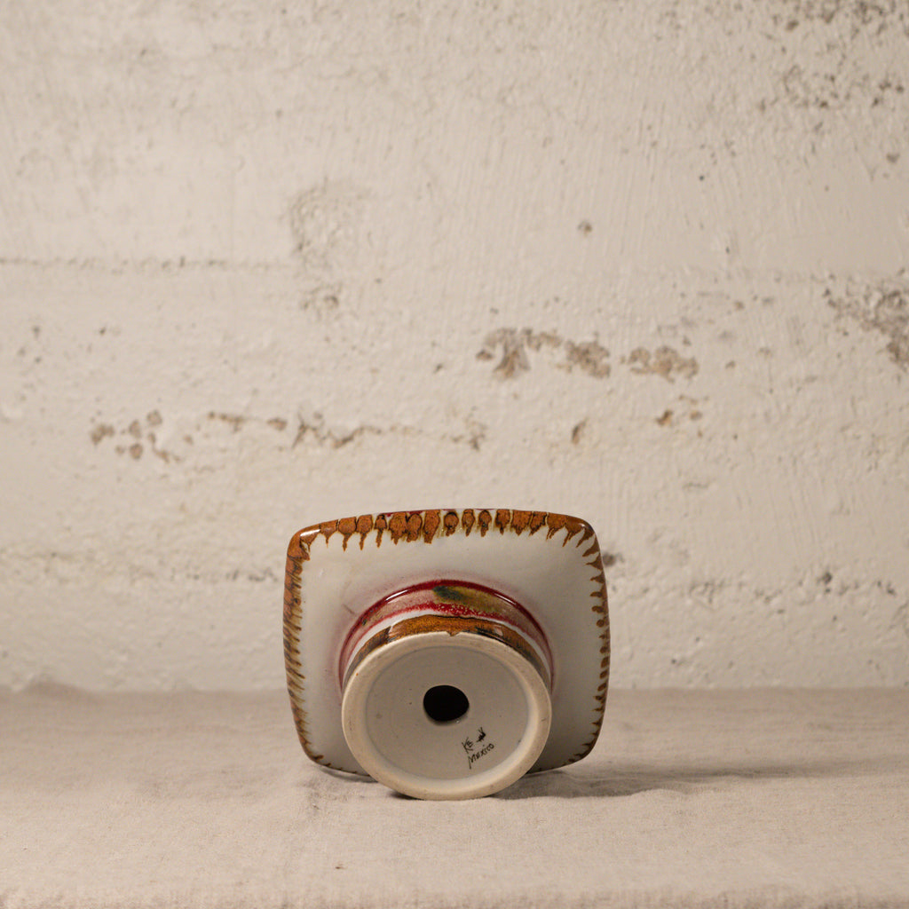 Small ceramic vase with decorative rim on a textured surface