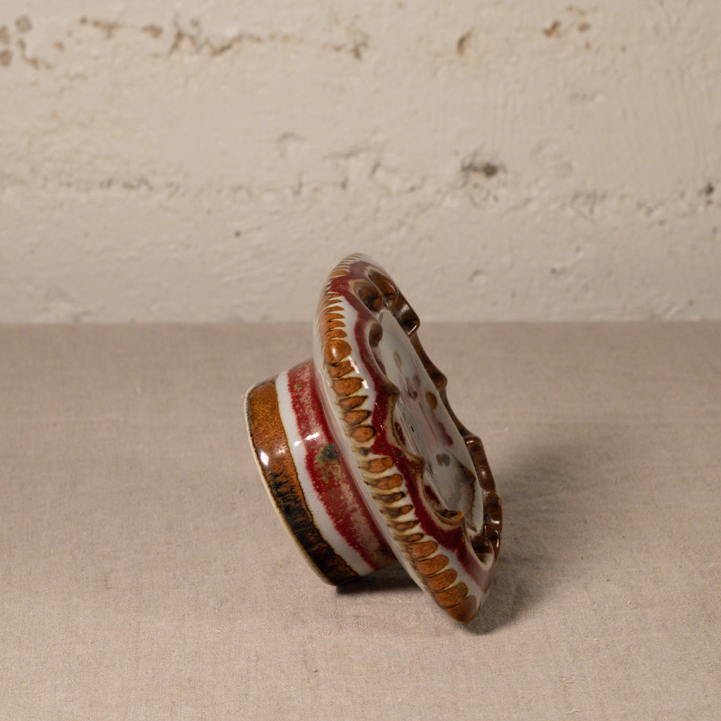 Decorative ceramic knob with red and gold patterns on a beige surface.