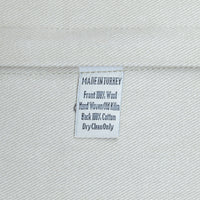 A close-up of a white woven fabric label sewn onto a light gray or off-white textile, showing text that reads 'MADE IN TURKEY', 'Front 100% Wool', 'Hand Woven Old Kilim', 'Back 100% Cotton', and 'DryCleanOnly'.