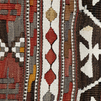 Close-up of a woven rug showing vertical geometric bands in cream, rust red, brown, black, gray, and small gold accents.