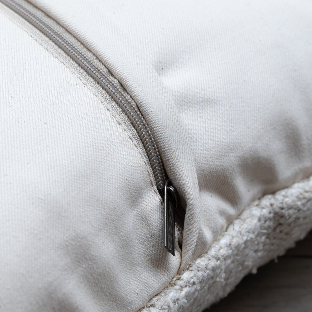 Close-up of a cream-colored fabric zippered cushion with a sherpa lining visible along the edge.