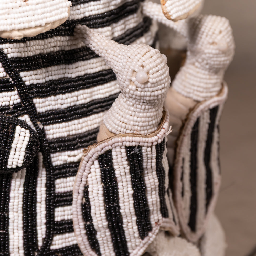 Close-up of a beaded textile or garment with black and off-white striped panels and small raised decorative elements, photographed against a soft neutral background.