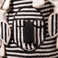 Close-up of a hand-beaded textile or bag featuring a stylized face design with black and off-white beadwork, striped horizontal bands, and leaf-like side motifs.