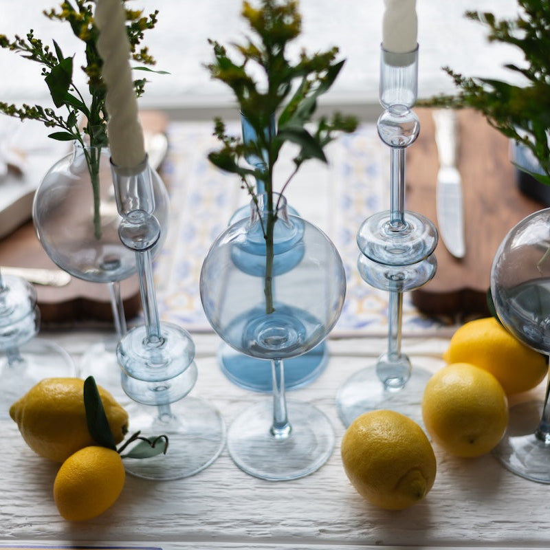 light blue glass candle holders with greenery and lemons on a wooden table.
