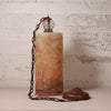A vintage-style table lamp with a cylindrical amber-brown marbled stone or resin column, a dark metal chain, a clear glass globe shade, and a matching round base, set against a distressed off-white wall.