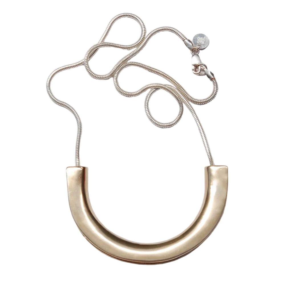 Gold necklace with a large curved pendant on a light gray background