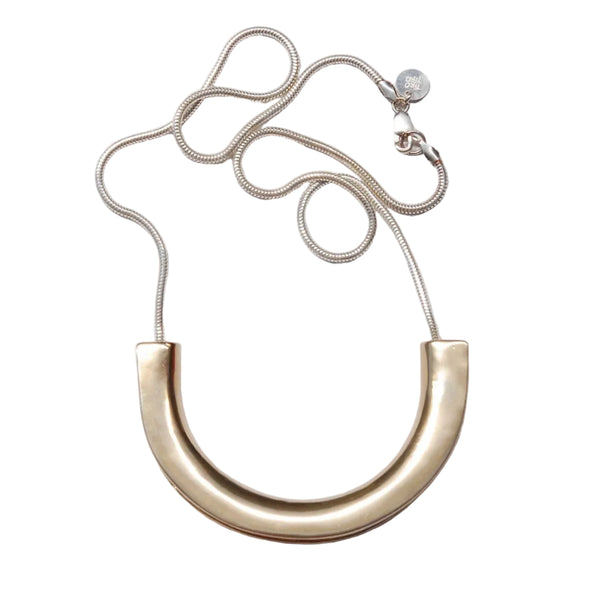 Gold necklace with a large curved pendant on a light gray background