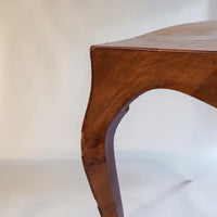 Close-up of a curved wooden table leg with a warm brown finish and visible wood grain, photographed against a plain light background.