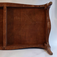 The underside of a rustic wooden table or shelf, showing curved brown wood grain, a central divider, and visible scratches on the inner panel.