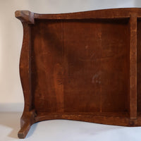 Close-up of the underside of a rustic wooden table or bench, showing the curved front apron, side supports, and visible pencil markings on the wood grain.