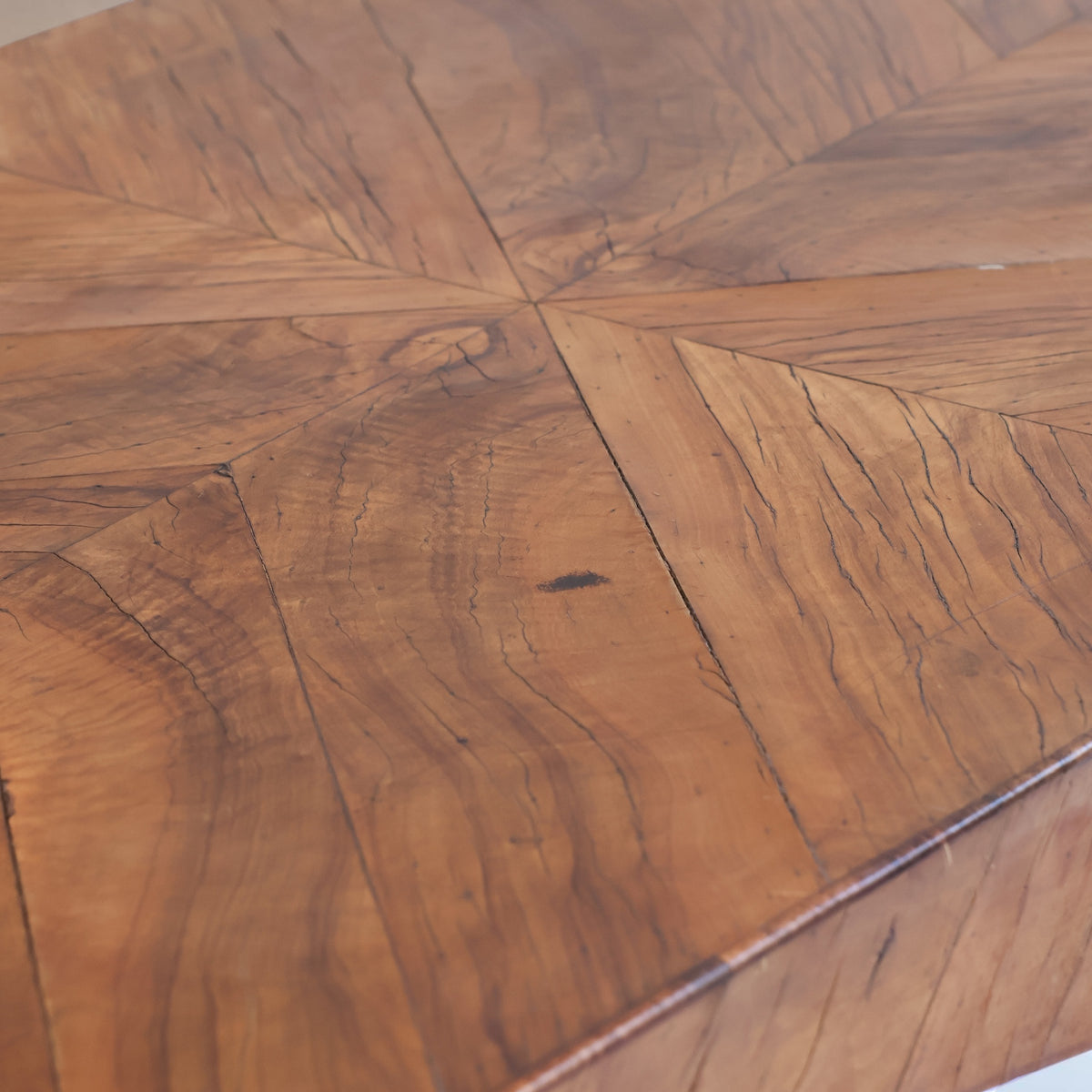 Close-up of a wooden table top with a geometric starburst inlay pattern made of curved wood panels in warm medium brown tones.