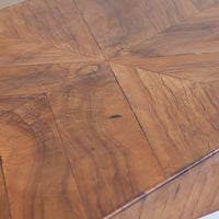 Close-up of a wooden table top with a geometric starburst inlay pattern made of curved wood panels in warm medium brown tones.