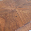 Close-up of a wooden table top with a geometric starburst inlay pattern made of curved wood panels in warm medium brown tones.
