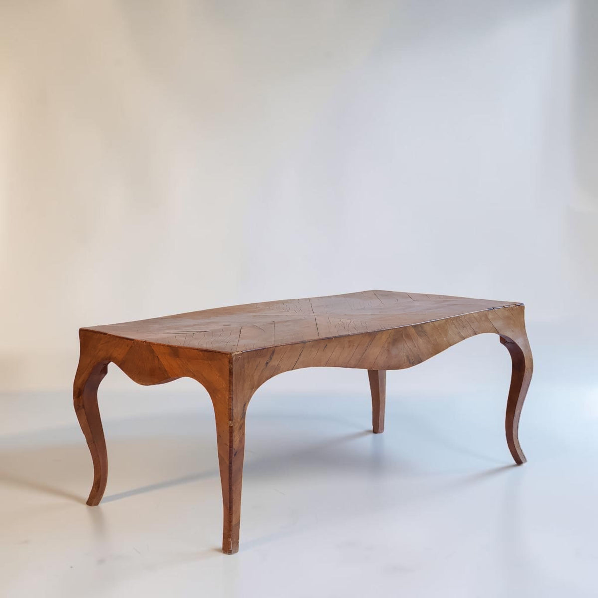A vintage wooden coffee table with a herringbone patterned top and curved cabriole-style legs, photographed against a plain off-white studio background.