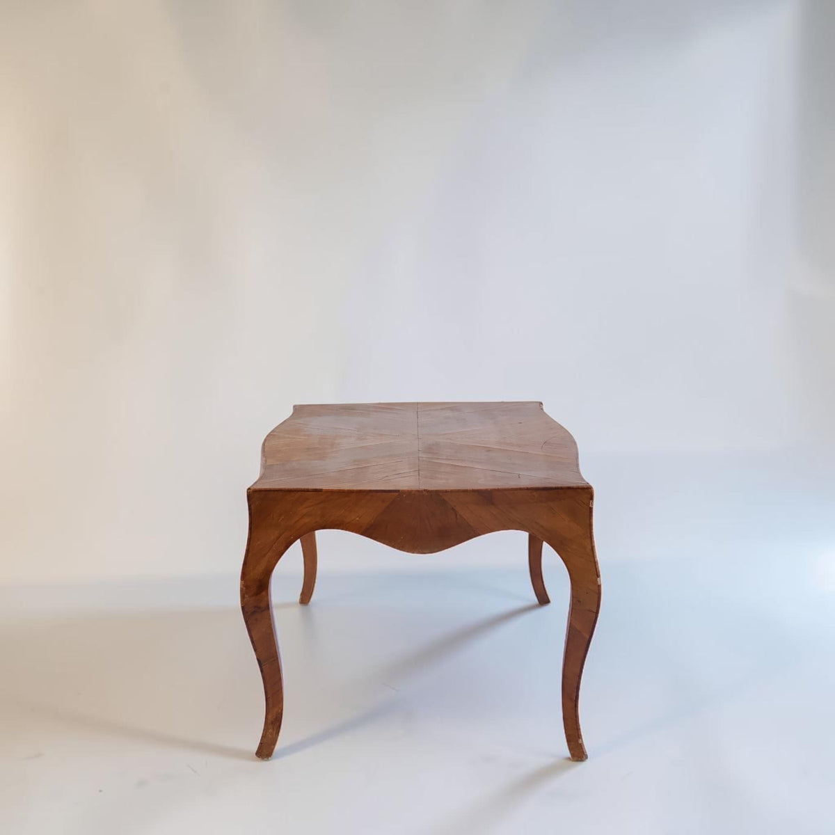A small wooden side table with a warm brown finish, featuring curved cabriole-style legs and a gently angled rectangular top, photographed against a plain off-white studio background.