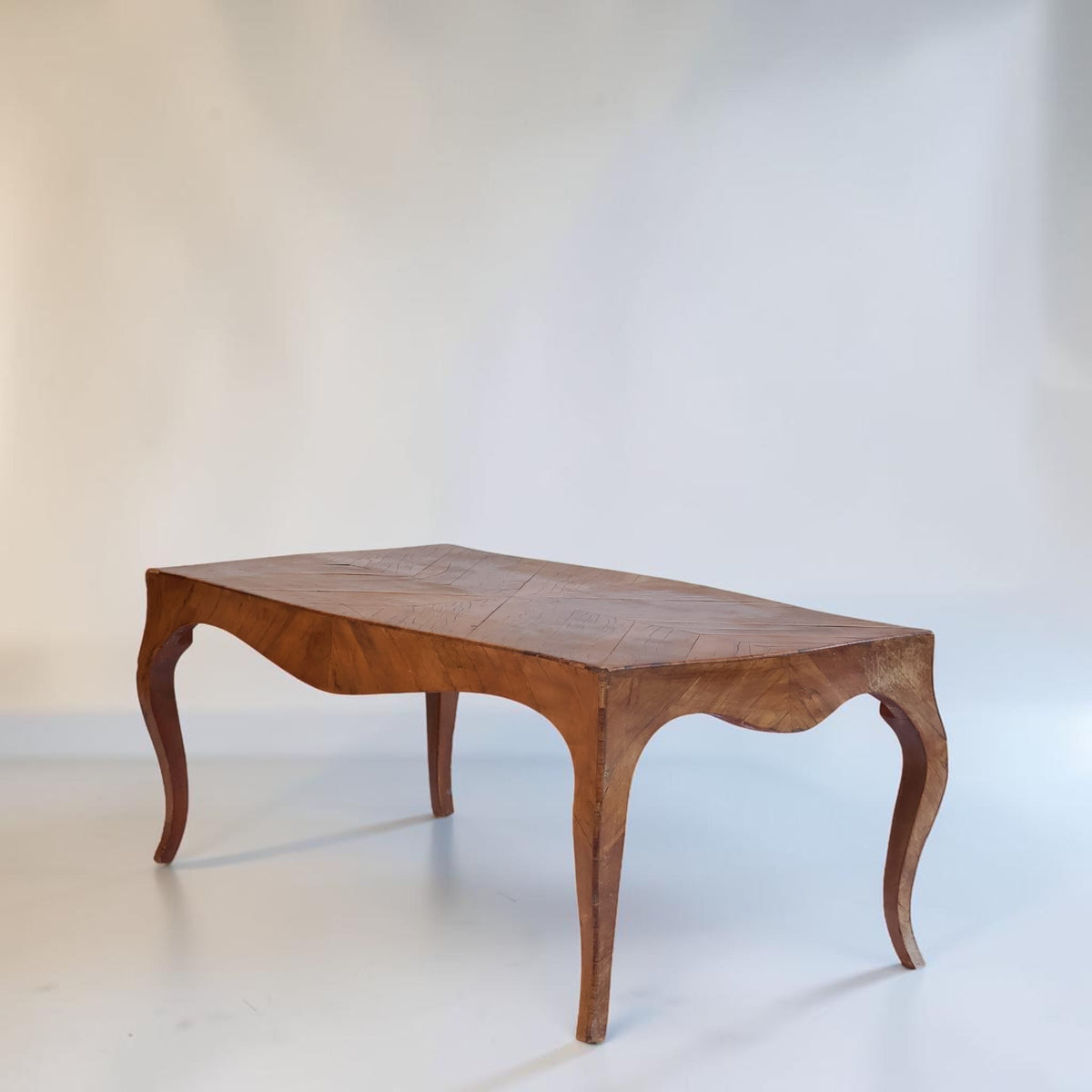 A mid-century wooden coffee table with a warm brown finish, featuring a curved apron, cabriole-style legs, and a segmented top, photographed against a neutral light gray studio backdrop.