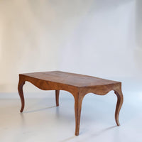 A mid-century wooden coffee table with a warm brown finish, featuring a curved apron, cabriole-style legs, and a segmented top, photographed against a neutral light gray studio backdrop.