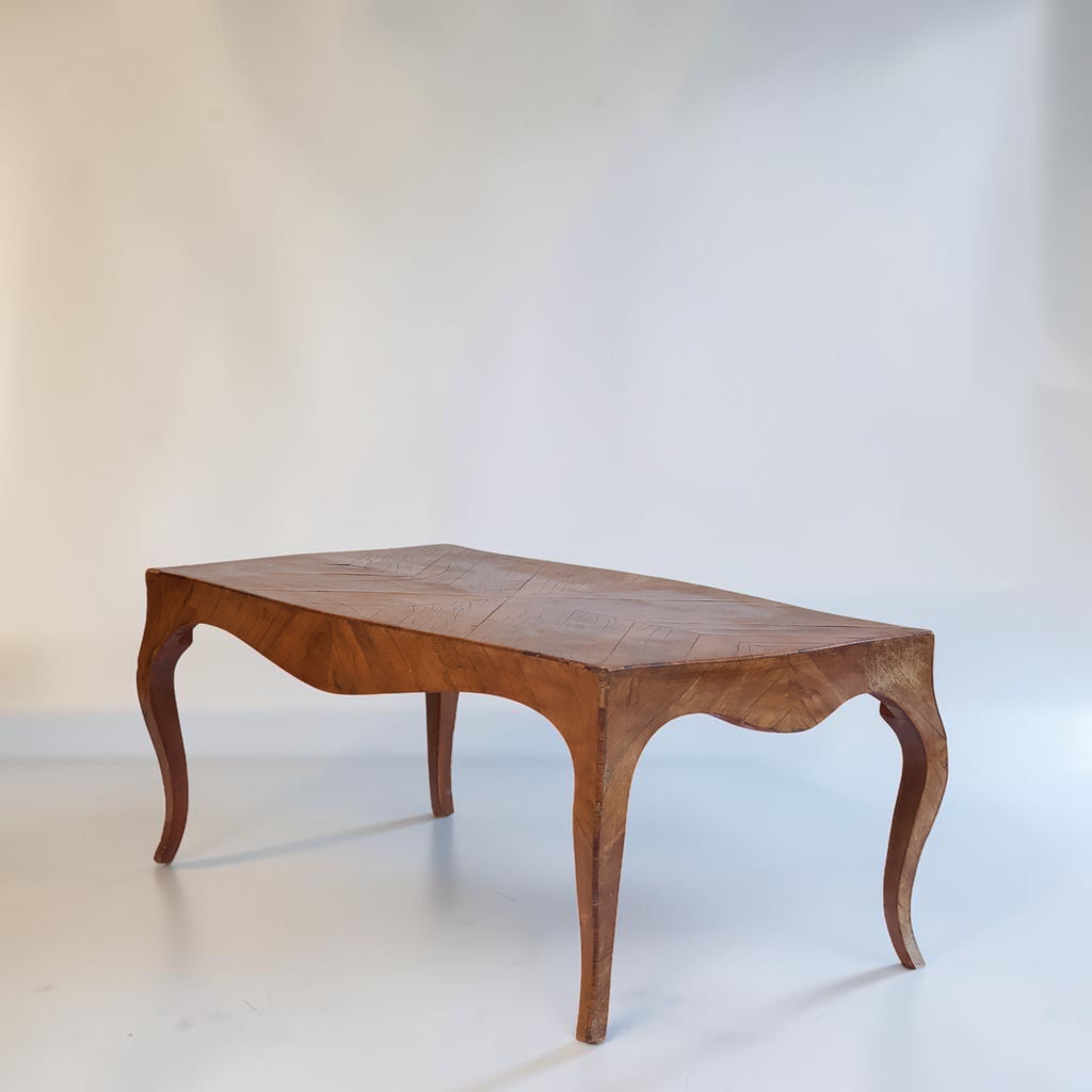 A mid-century wooden coffee table with a warm brown finish, featuring a curved apron, cabriole-style legs, and a segmented top, photographed against a neutral light gray studio backdrop.