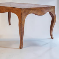 A close-up studio shot of an antique wooden table leg with a curved cabriole-style leg and visible wood grain patterns, set against a plain white background.