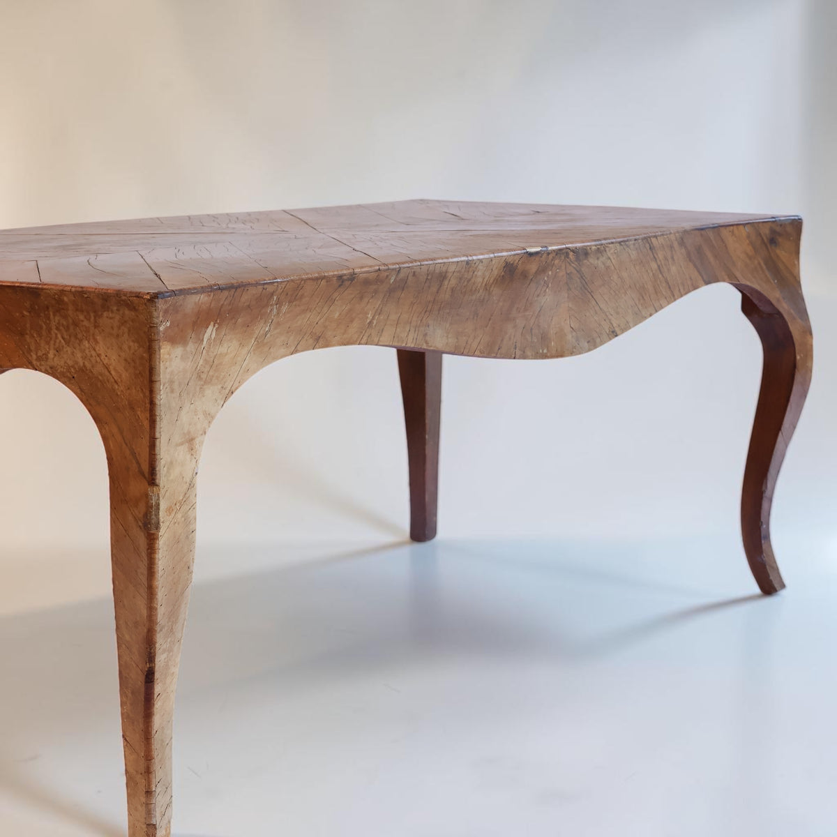 A rustic wooden table with a curved apron and cabriole-style legs, shown against a plain off-white background.