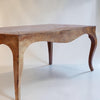 A rustic wooden table with a curved apron and cabriole-style legs, shown against a plain off-white background.