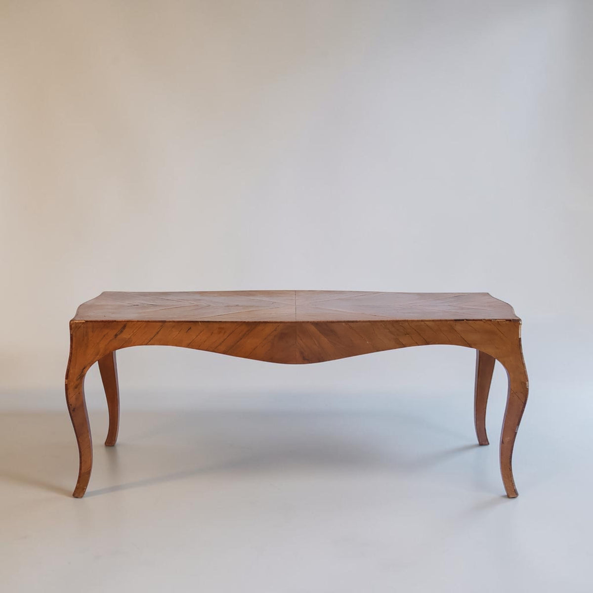 A mid-century wooden console table with a curved apron and cabriole legs, shown against a plain off-white studio background.