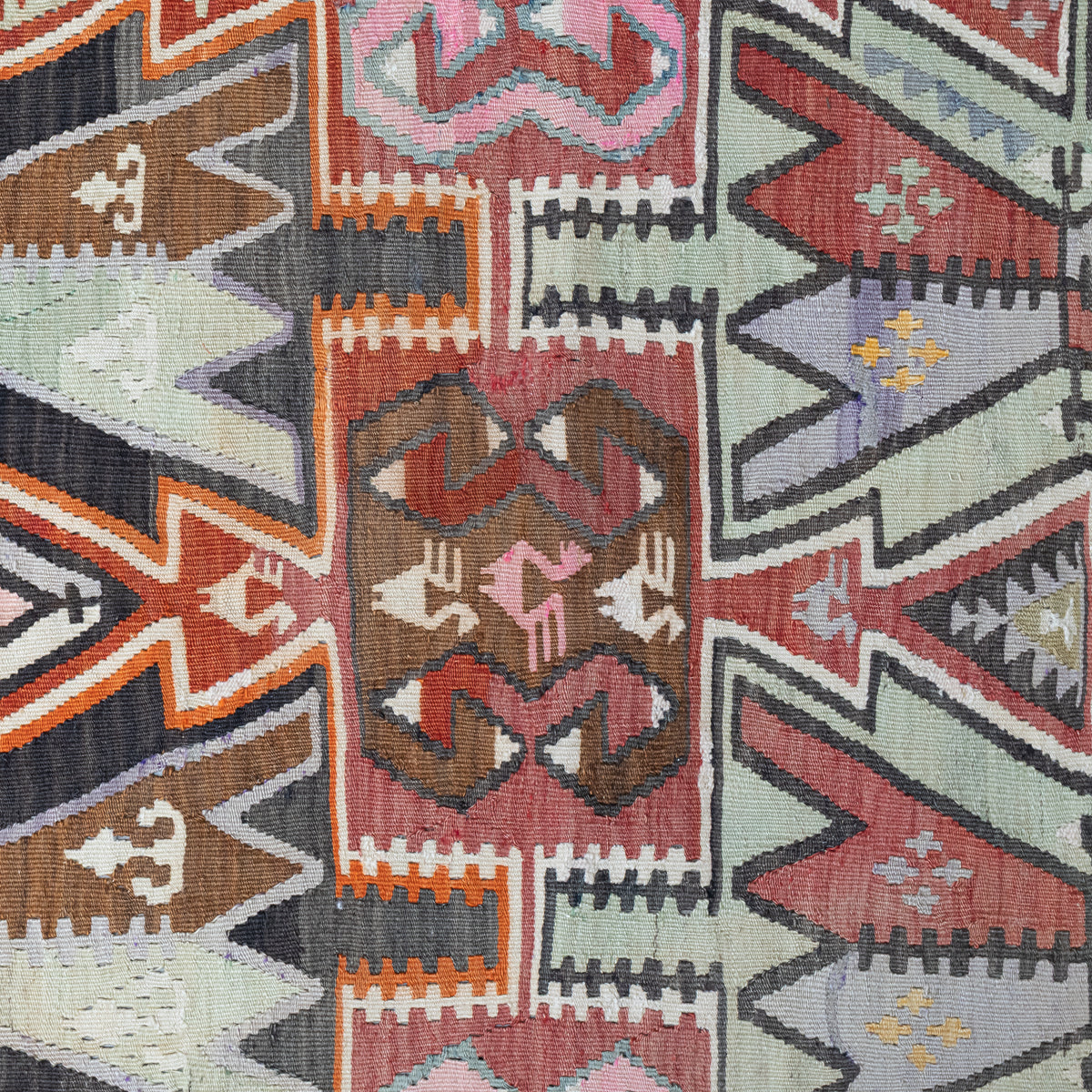 A close-up of a woven kilim textile with a geometric pattern in muted red, brown, gray, black, orange, and pale green.