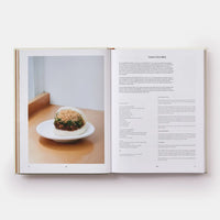 Open book showing a photograph of a dish on a wooden table with text on a white background
