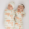 Two babies wearing matching outfits with orange and green patterns on a plain background