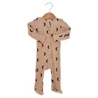A baby footed one-piece sleeper in beige with a black crescent moon pattern, hanging on a wooden hanger against a white background.