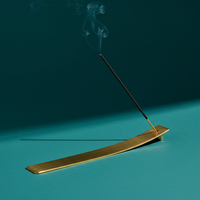 Gold incense burner with a single incense stick on a teal background
