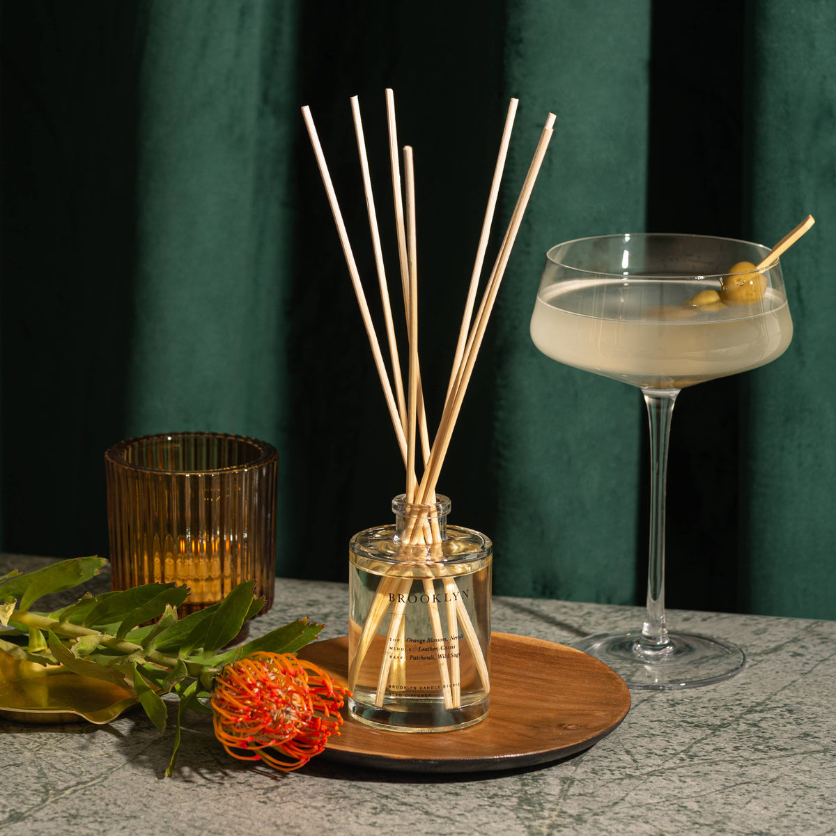 Reed diffuser with decorative sticks on a table against a dark green curtain background
