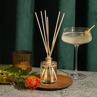 Reed diffuser with decorative sticks on a table against a dark green curtain background