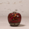 A small hand-painted ceramic pot with a lid, featuring a red and brown bird design with black accents, set against a neutral textured background.