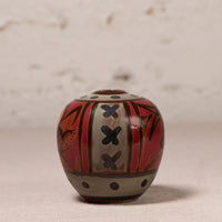 A small hand-painted ceramic pot with a rounded body, featuring a red and beige pattern with black accents, set against a neutral textured background.