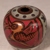 A round ceramic vase with a glossy finish, featuring a stylized bird design in brown and orange on a red background, with a cream-colored top band decorated with dark blue dots.