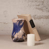 Vase with blue and beige design, book, and candle on a textured surface