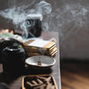 Incense burning in a small dish with smoke rising, on a wooden surface.