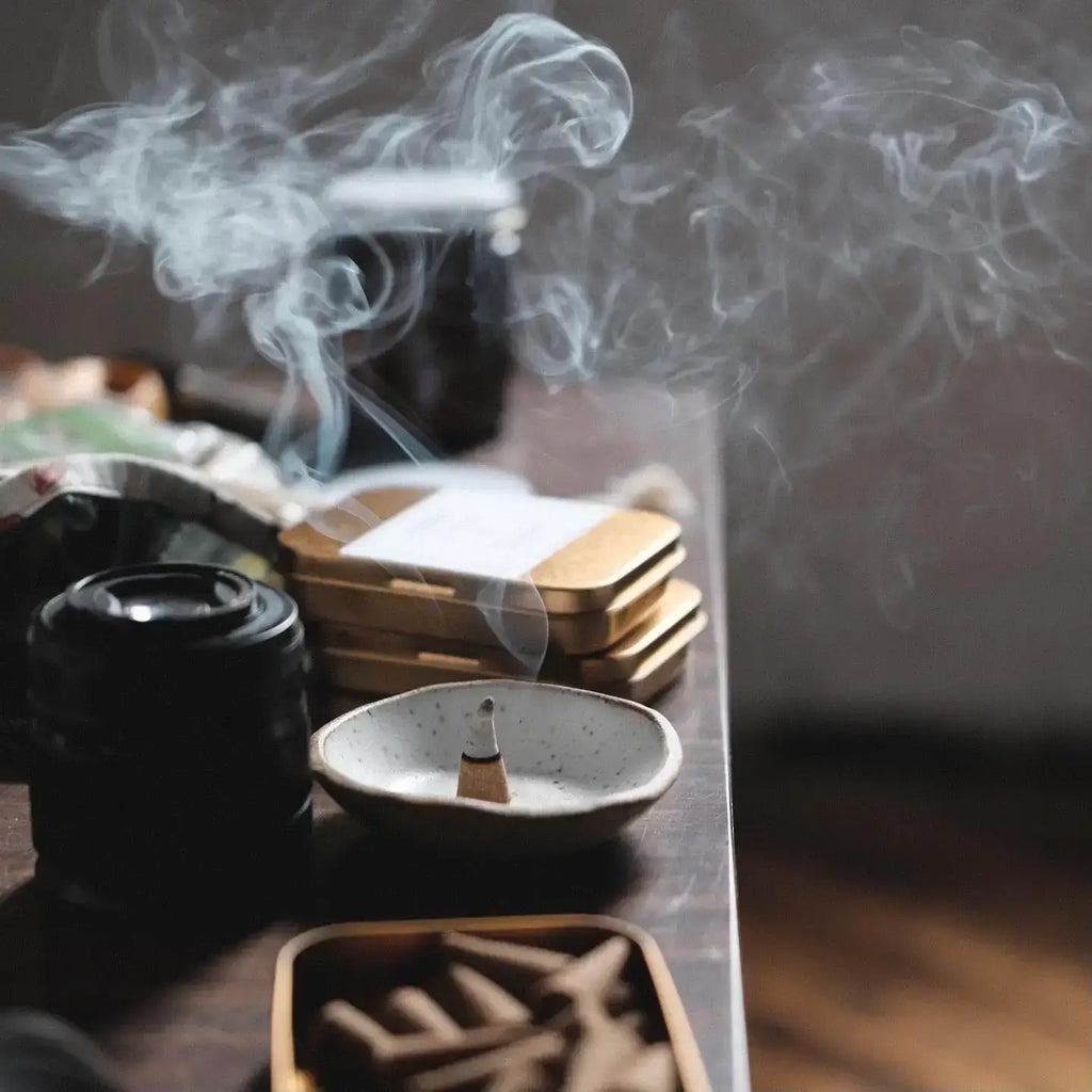 Incense burning in a small dish with smoke rising, on a wooden surface.
