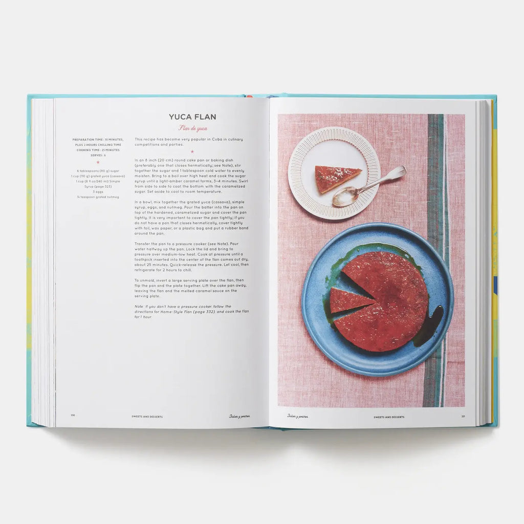An open cookbook spread showing a recipe for Yuca Flan, with printed text on the left page and a food photograph of a sliced red-pink dessert on a blue plate on the right page, photographed on a light gray background.