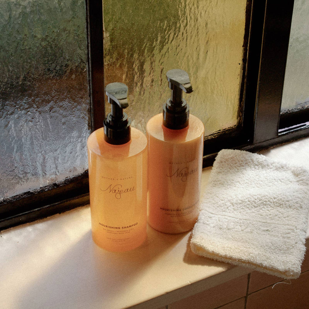 Two bottles of shampoo on a windowsill with a towel nearby
